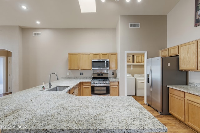 10187 E Watson Dr, Tucson, AZ 85730 - kitchen featuring appliances with stainless steel finishes, a sink, washer and dryer, light wood finished floors, and arched walkways