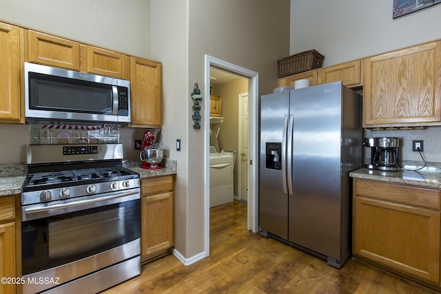 kitchen with washer and clothes dryer, light stone counters, wood finished floors, appliances with stainless steel finishes, and brown cabinetry