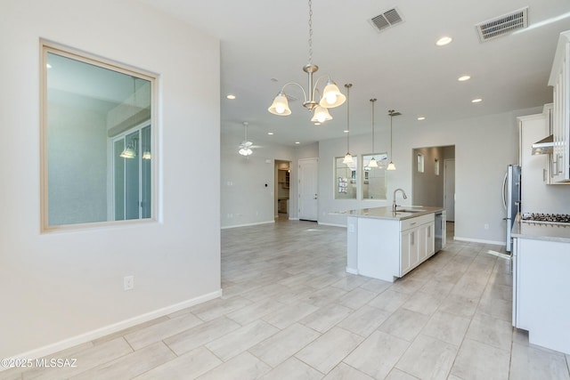 kitchen featuring white cabinets, ceiling fan with notable chandelier, hanging light fixtures, an island with sink, and stainless steel appliances