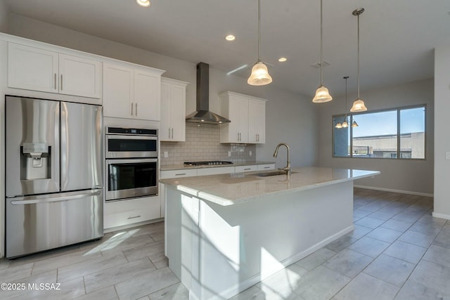 kitchen featuring sink, wall chimney exhaust hood, stainless steel appliances, an island with sink, and white cabinets