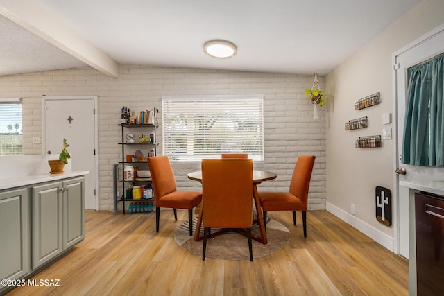 dining room with light wood-type flooring, lofted ceiling with beams, and brick wall