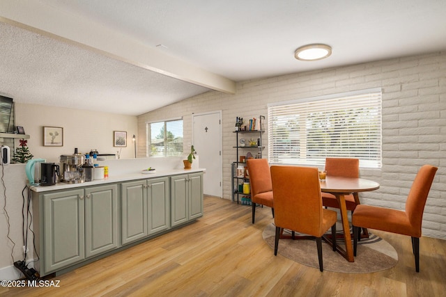 dining room with brick wall, lofted ceiling with beams, light wood-type flooring, and a wealth of natural light