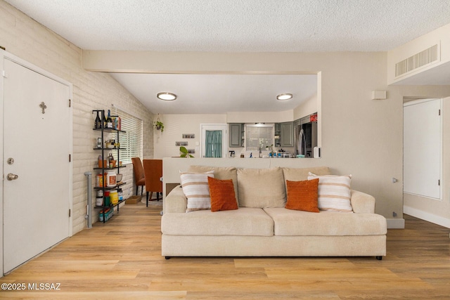 living room featuring a textured ceiling, hardwood / wood-style floors, vaulted ceiling with beams, and brick wall