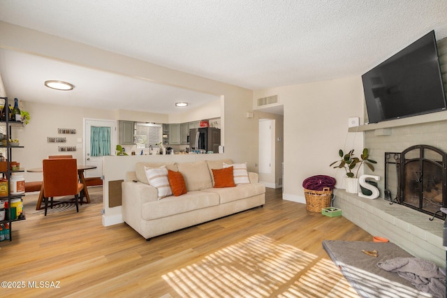 living room featuring a brick fireplace, light wood-type flooring, and a textured ceiling