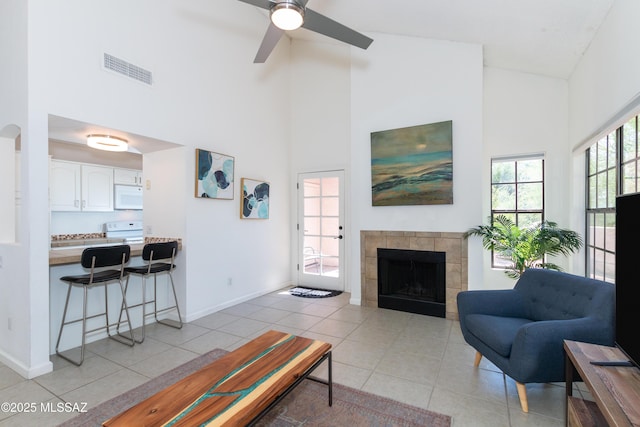 tiled living room featuring ceiling fan, a towering ceiling, and a tiled fireplace