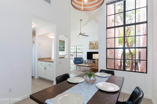 dining area with ceiling fan, light tile patterned floors, and a towering ceiling