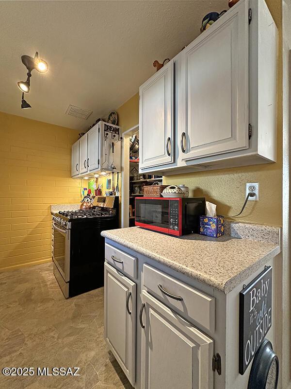 kitchen featuring white cabinets, rail lighting, brick wall, and gas range