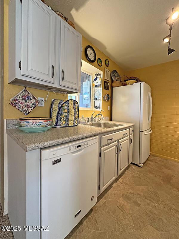 kitchen with white cabinetry, white appliances, sink, and brick wall