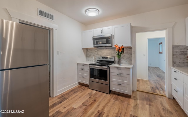 kitchen with backsplash, white cabinets, light hardwood / wood-style floors, and appliances with stainless steel finishes