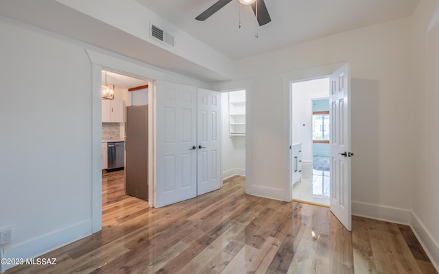 unfurnished bedroom with light wood-type flooring, ceiling fan, a spacious closet, stainless steel refrigerator, and a closet