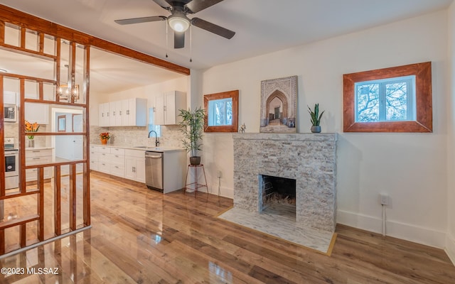 living room featuring light wood-type flooring, a stone fireplace, ceiling fan, and sink