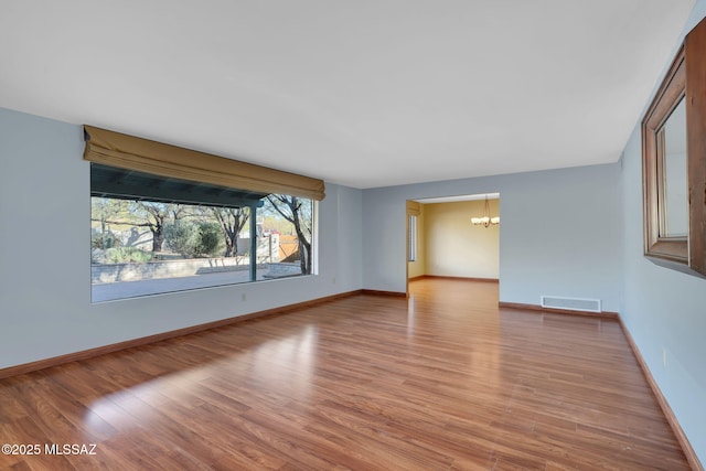 spare room featuring a notable chandelier and light hardwood / wood-style flooring