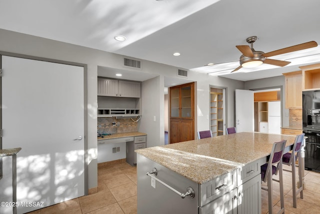 kitchen with a center island, tasteful backsplash, ceiling fan, light stone counters, and light tile patterned floors