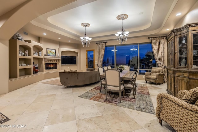 dining room with a tray ceiling, built in shelves, light tile patterned floors, and an inviting chandelier