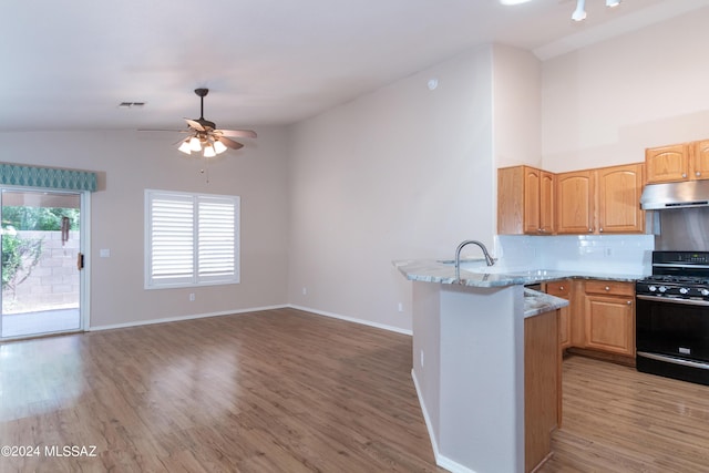 kitchen with lofted ceiling, a peninsula, light wood-type flooring, under cabinet range hood, and gas stove