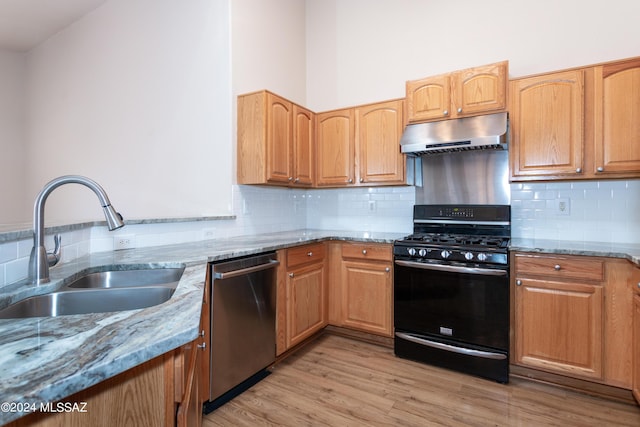 kitchen with dishwasher, black gas range, sink, light hardwood / wood-style flooring, and light stone countertops