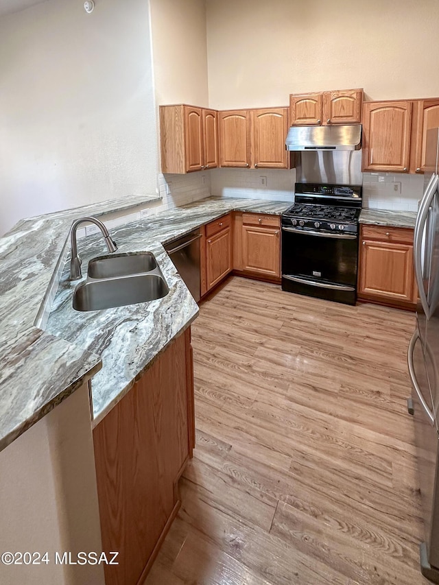 kitchen with sink, stainless steel appliances, light stone counters, kitchen peninsula, and light hardwood / wood-style floors