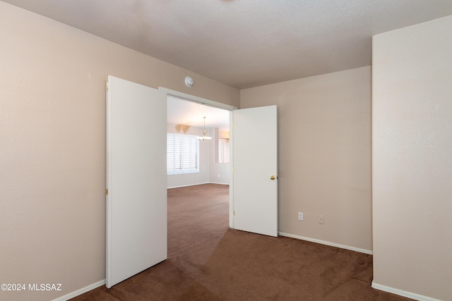 carpeted spare room with an inviting chandelier and baseboards