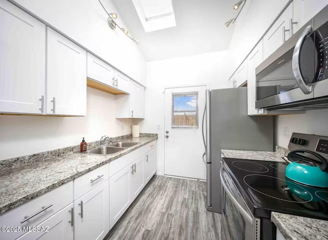 kitchen with white cabinetry, appliances with stainless steel finishes, lofted ceiling with skylight, sink, and light hardwood / wood-style flooring