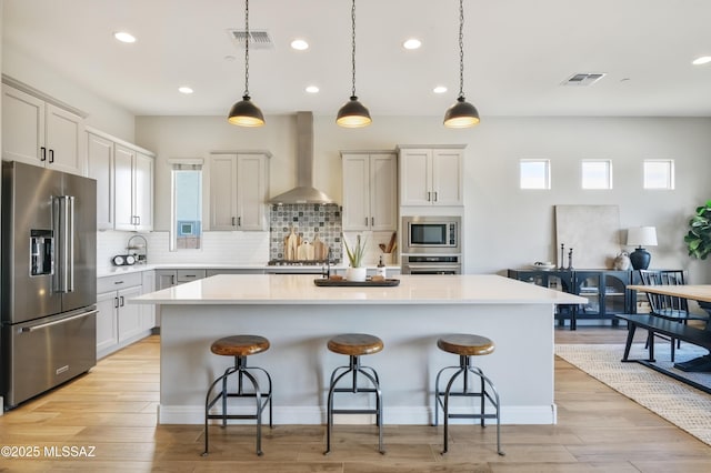 kitchen featuring hanging light fixtures, a kitchen island, stainless steel appliances, and wall chimney exhaust hood