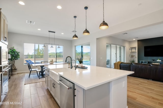 kitchen with sink, a center island with sink, stainless steel dishwasher, and pendant lighting