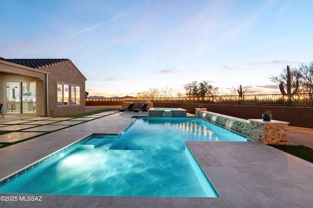 pool at dusk featuring pool water feature, an in ground hot tub, and a patio area