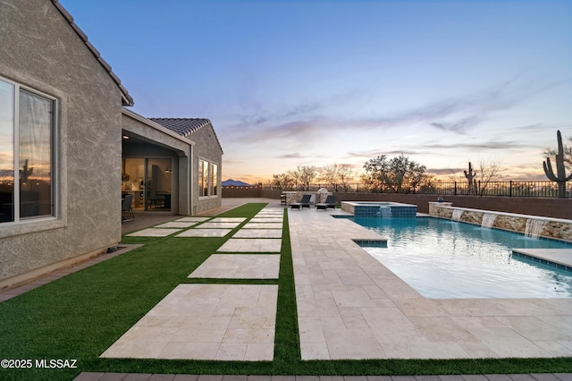 pool at dusk with an in ground hot tub, pool water feature, and a patio area