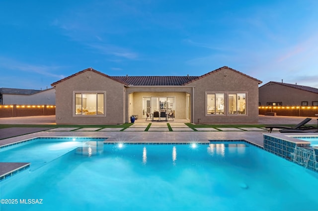 pool at dusk featuring a patio and a jacuzzi