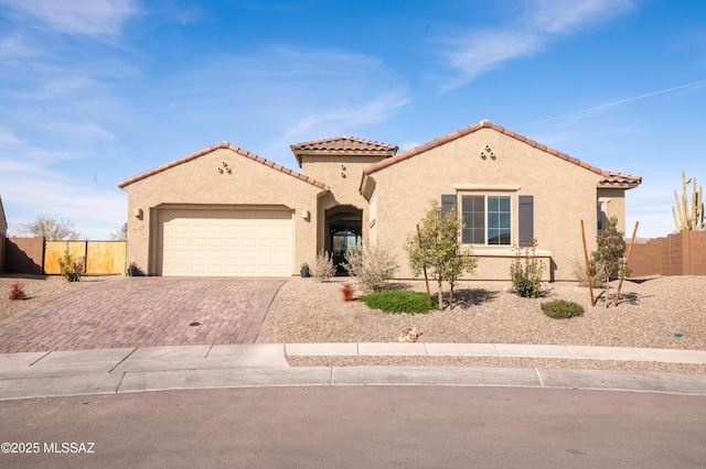 mediterranean / spanish-style house with a tile roof, stucco siding, fence, an attached garage, and decorative driveway