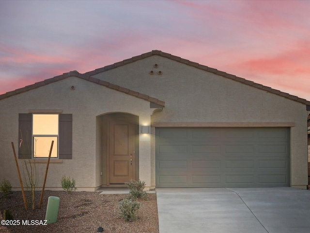 view of front of home featuring a garage, concrete driveway, a tiled roof, and stucco siding