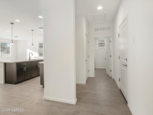 hall featuring baseboards, visible vents, light wood-type flooring, a sink, and recessed lighting