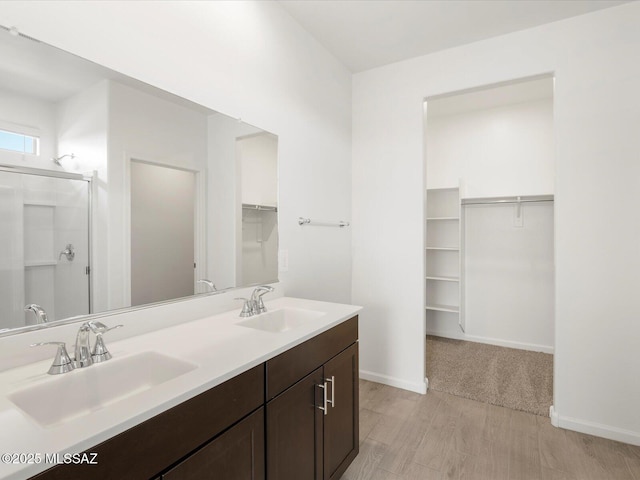 bathroom featuring a spacious closet, double vanity, a sink, and baseboards