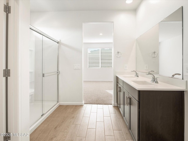 full bathroom with double vanity, a sink, a shower stall, wood finished floors, and baseboards