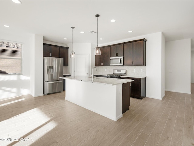 kitchen featuring dark brown cabinets, appliances with stainless steel finishes, light wood-style floors, and tasteful backsplash