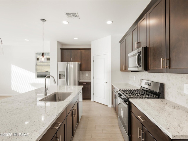 kitchen featuring light stone counters, dark brown cabinetry, stainless steel appliances, a sink, and visible vents