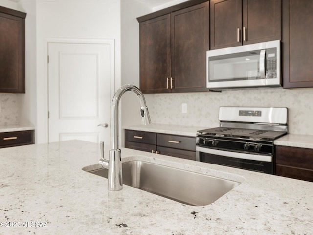 kitchen with light stone counters, tasteful backsplash, appliances with stainless steel finishes, a sink, and dark brown cabinets