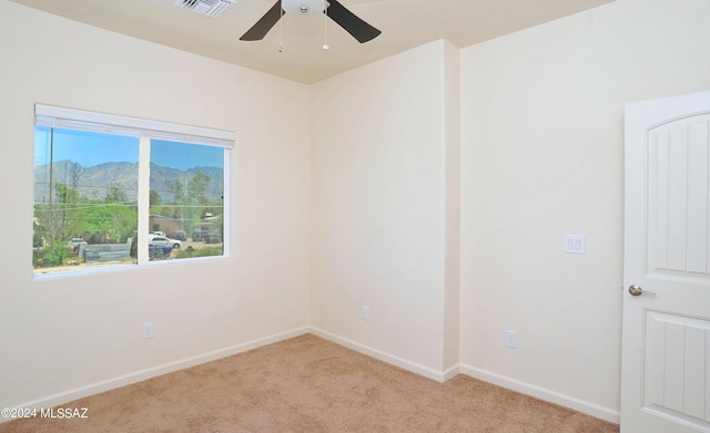 unfurnished room with a mountain view, ceiling fan, and light carpet