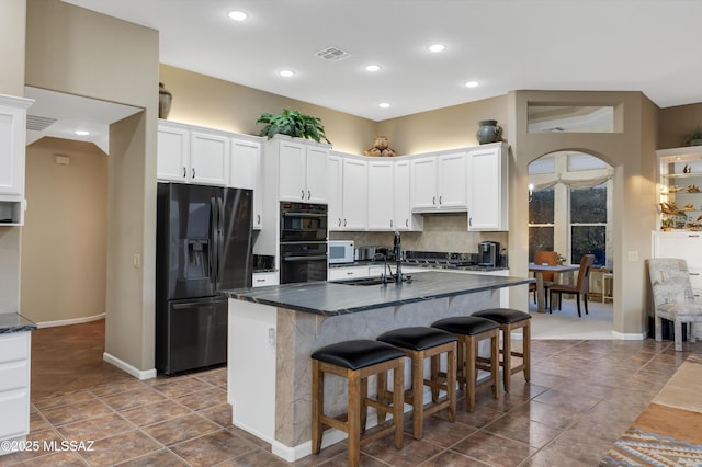 kitchen featuring a kitchen island with sink, a sink, white cabinets, black appliances, and dark countertops