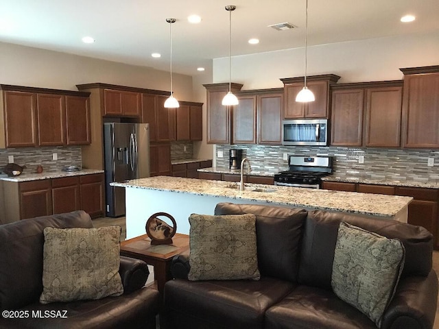 kitchen with backsplash, stainless steel appliances, sink, hanging light fixtures, and an island with sink