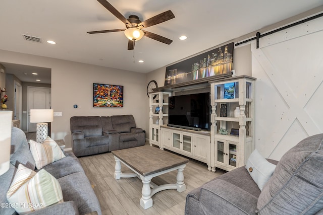 living room featuring ceiling fan, a barn door, and light wood-type flooring