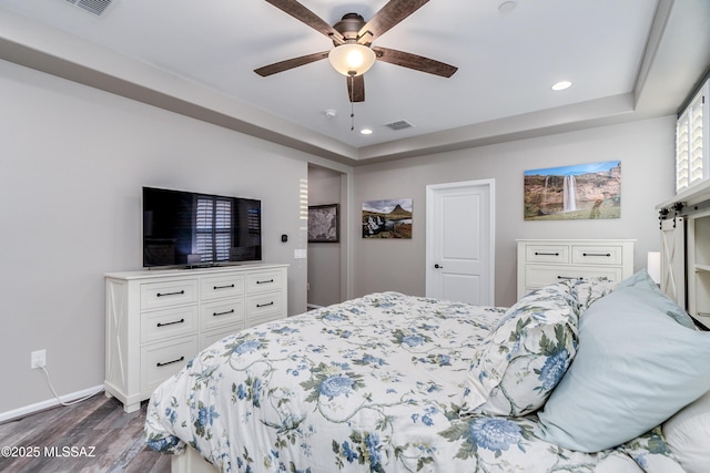 bedroom with ceiling fan, a tray ceiling, and dark hardwood / wood-style flooring