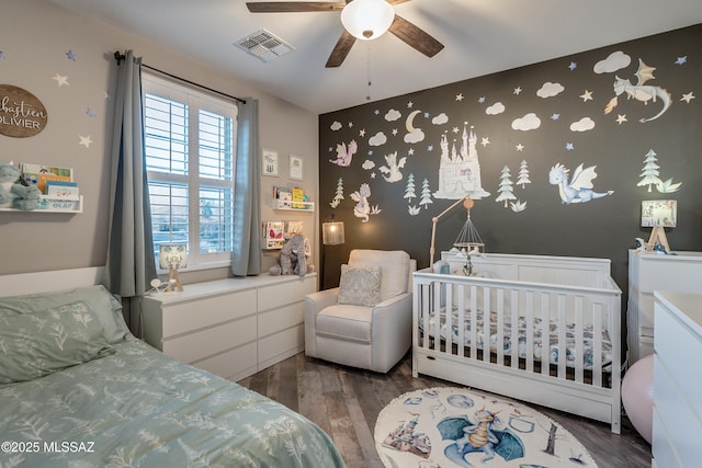 bedroom with ceiling fan, dark hardwood / wood-style floors, and a crib