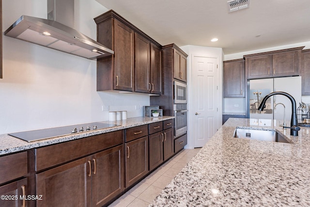 kitchen featuring visible vents, dark brown cabinetry, a sink, oven, and wall chimney exhaust hood