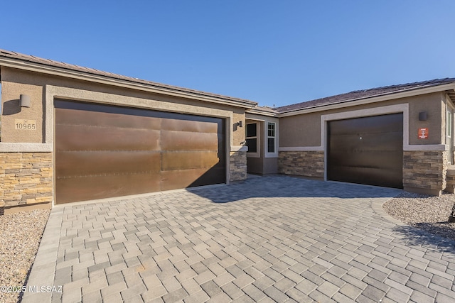 view of front of property with decorative driveway, stone siding, a garage, and stucco siding