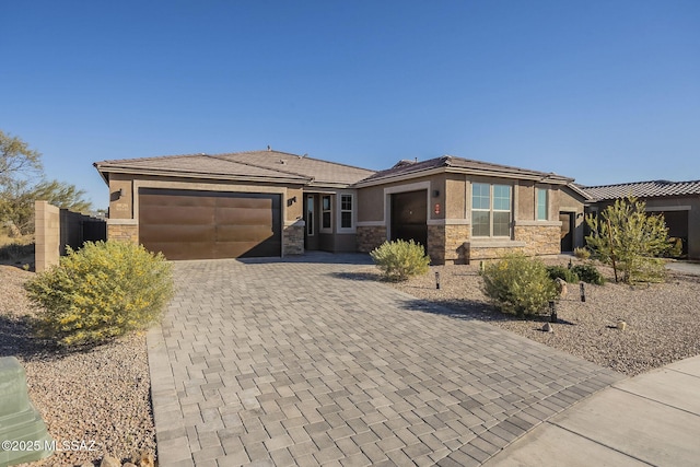 prairie-style home with stone siding, decorative driveway, an attached garage, and stucco siding