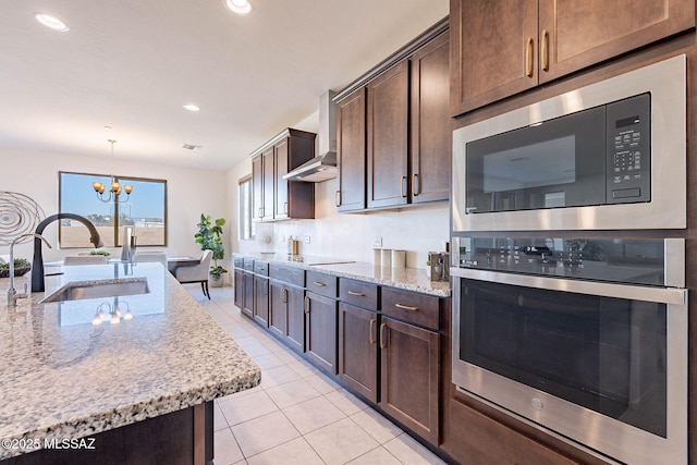 kitchen featuring dark brown cabinetry, built in microwave, wall chimney range hood, a sink, and light tile patterned flooring