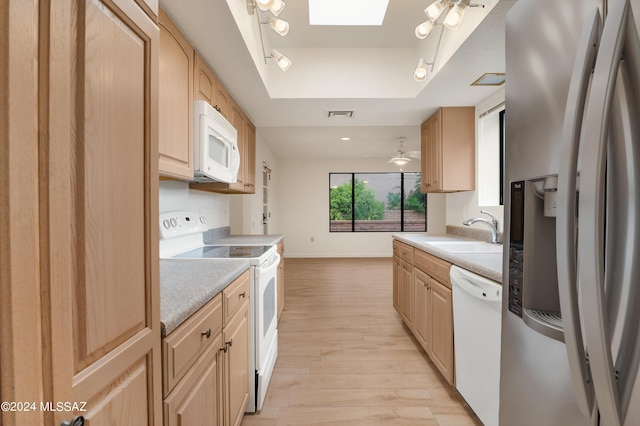 kitchen with white appliances, sink, light brown cabinetry, and a skylight