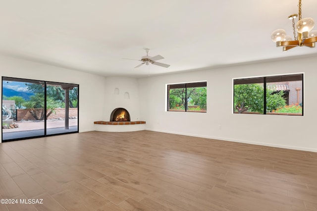 unfurnished living room featuring a wealth of natural light, ceiling fan with notable chandelier, and light wood-type flooring