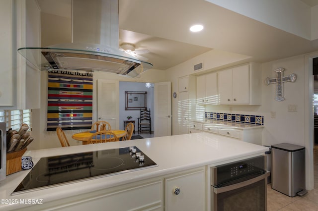 kitchen with island range hood, white cabinets, black electric stovetop, stainless steel oven, and light tile patterned floors