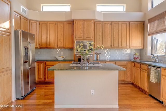 kitchen featuring sink, light hardwood / wood-style flooring, appliances with stainless steel finishes, tasteful backsplash, and a kitchen island